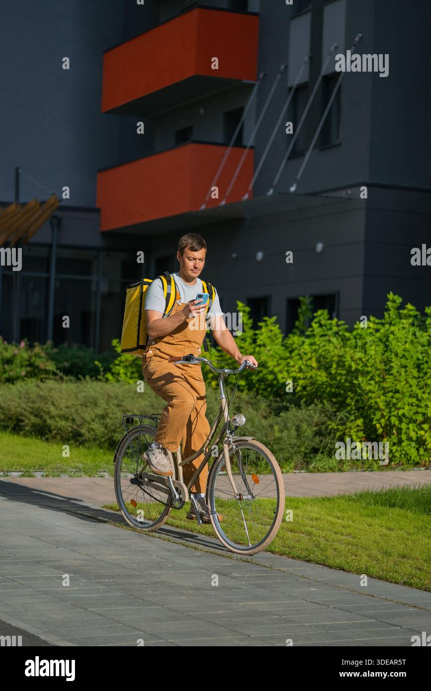 Fahrradkurier, der Lebensmittel auf einem Fahrrad in einer urbanen Umgebung liefert, auf einem Mobiltelefon nach Wegbeschreibungen sucht, repräsentiert die Gig Economy und den modernen Lieferservice Stockfoto
