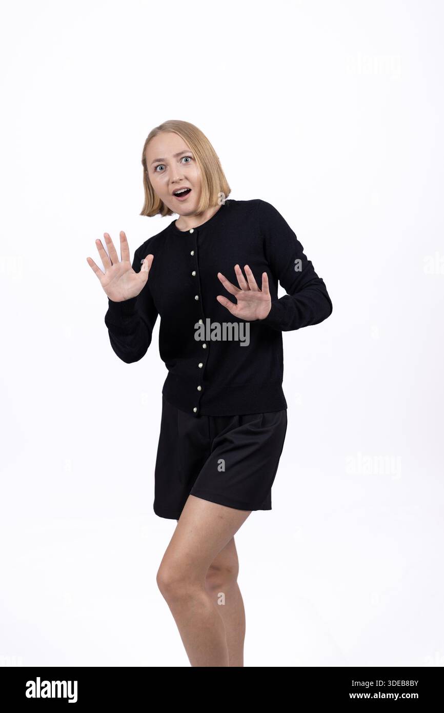 Verängstigte oder überraschte Frau, die in einem schwarzen Kleid zurückschreckt. Stockfoto