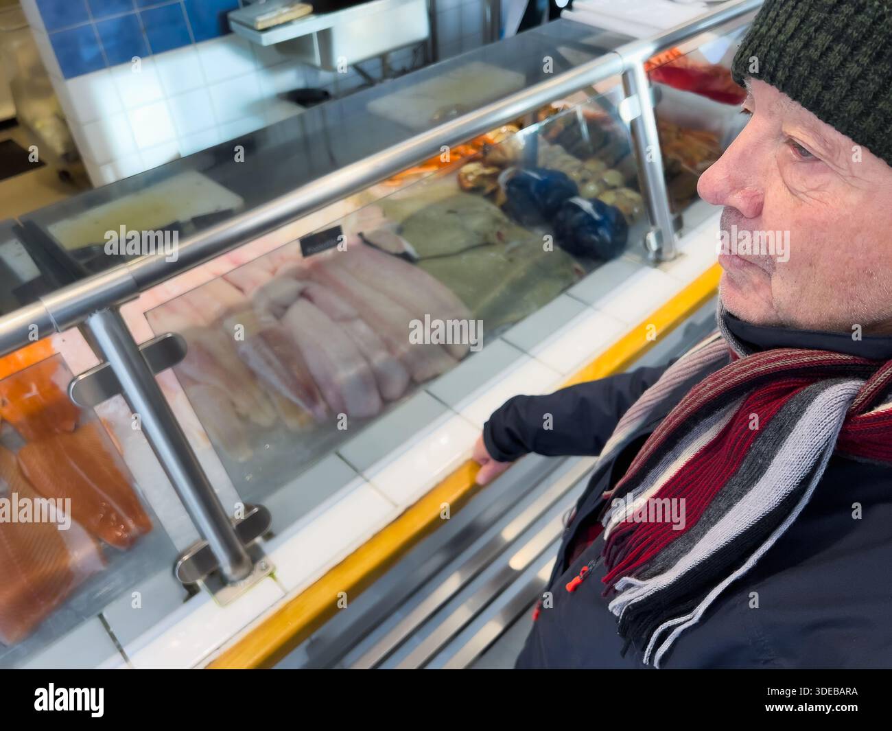 Langsam lebender Alltagsstil reifer Lebensstil mit einem älteren Mann, der frischen Fisch an einer Markttheke im Haus auswählt, ruhiger, fokussierter Ausdruck, einfache Routine Stockfoto
