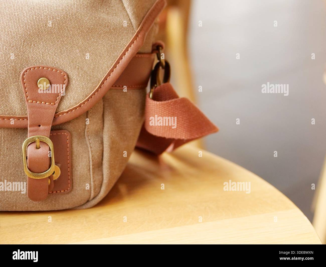 Nahaufnahme einer Vintage Canvas Umhängetasche mit Lederriemen und Messingschnalle auf Holzstuhl, Retro-Schultertasche, stilvolles Reiseaccessoire. Stockfoto