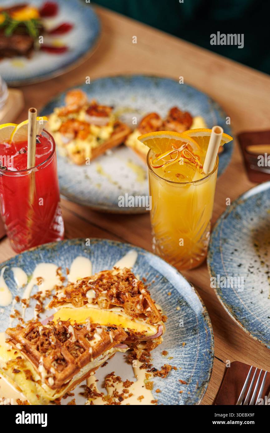 In einem belebten Restaurant werden während des Brunch verschiedene Gerichte serviert, darunter Waffeln mit Obst, frische Salate und bunte Getränke. Stockfoto