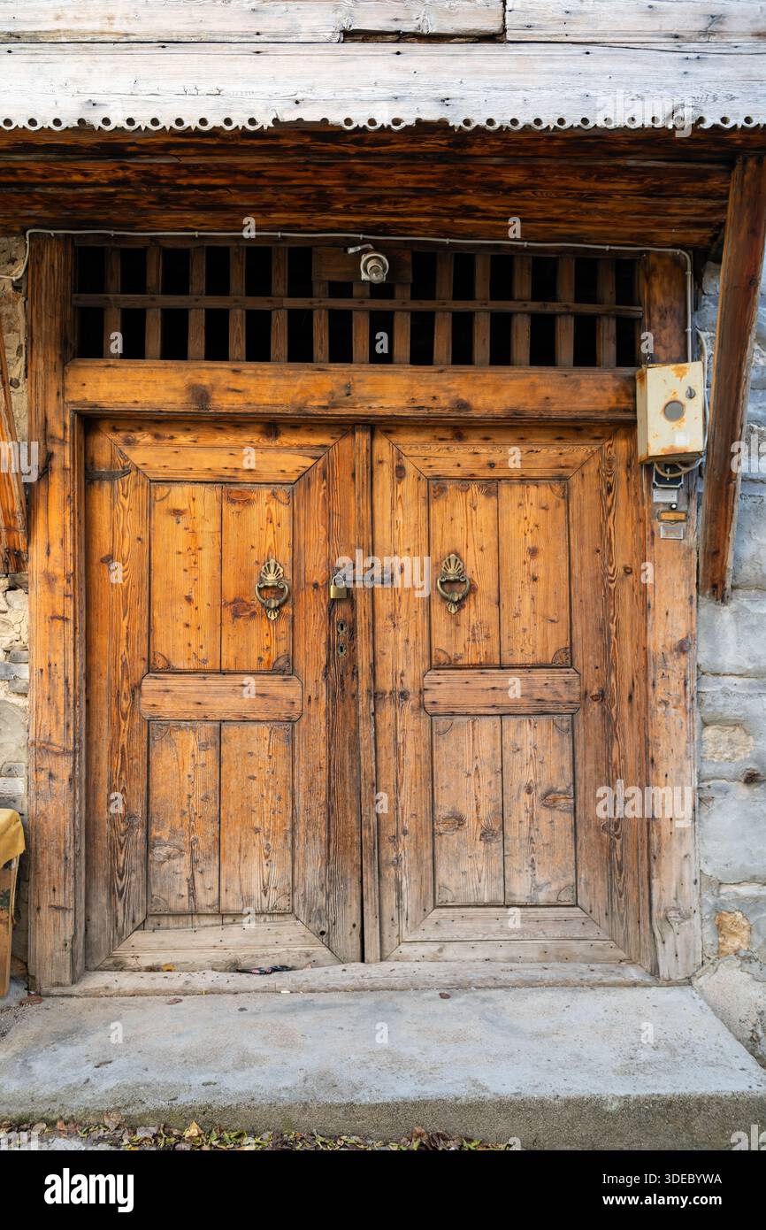 Eine traditionelle doppelflügelige Holztür eines historischen Steinhauses mit gehämmerten und handgeschnitzten Motiven aus Reiskorn. Stockfoto