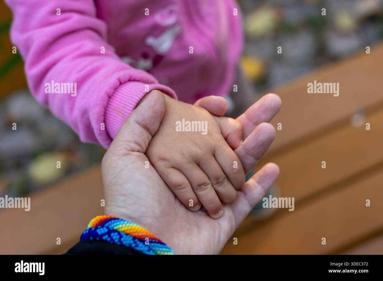 Nahaufnahme eines kleinen Kindes, das die Hand eines Erwachsenen im Freien hält, symbolisiert Vertrauen, Fürsorge und familiäre Verbindung, mit geringer Schärfentiefe und Wärme Stockfoto