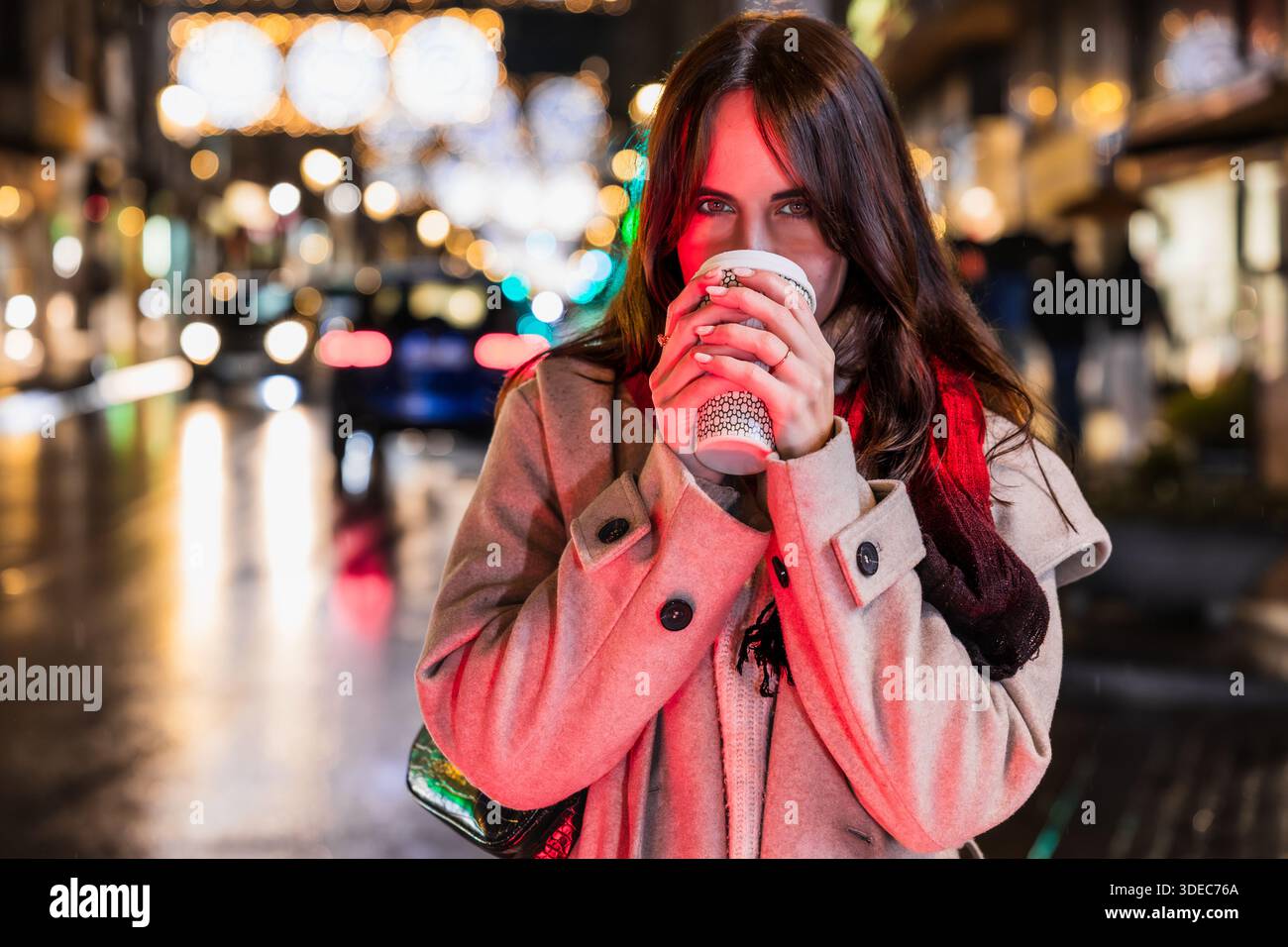 Frau trinkt nachts warmen Kaffee auf der Stadtstraße Stockfoto
