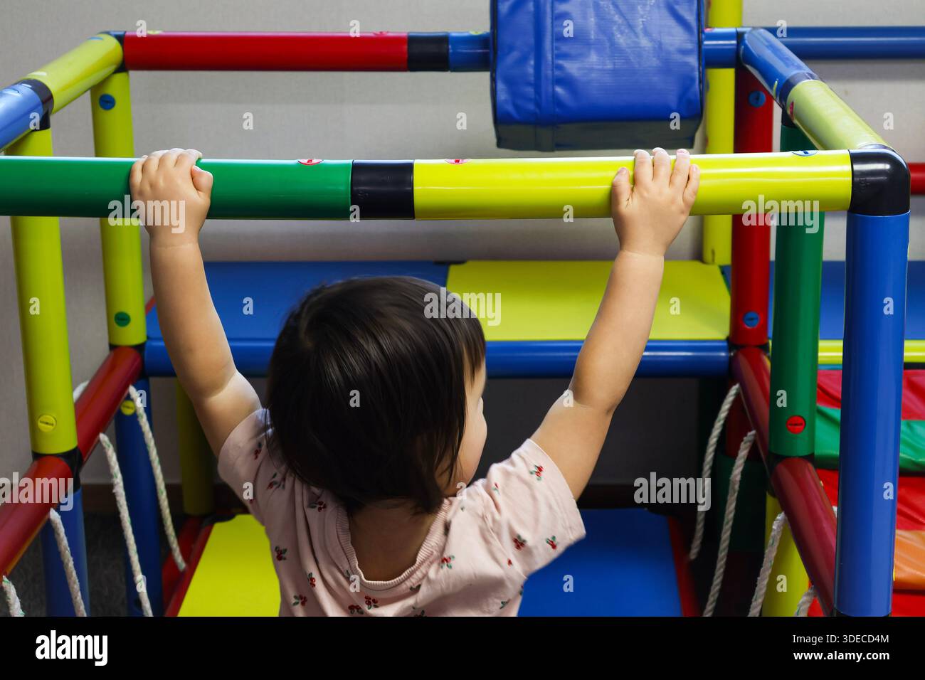 Aktives Kleinkind, das auf einem farbenfrohen Spielplatz hängt, entwickelt motorische Fähigkeiten und Kraft Stockfoto