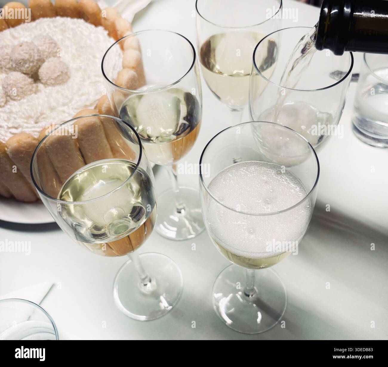 Das Bild zeigt eine Feier oder ein geselliges Treffen mit Gläsern Sekt, die in Gläser gegossen werden, und einem charlotte-Kuchen oder Tiramisu. Stockfoto