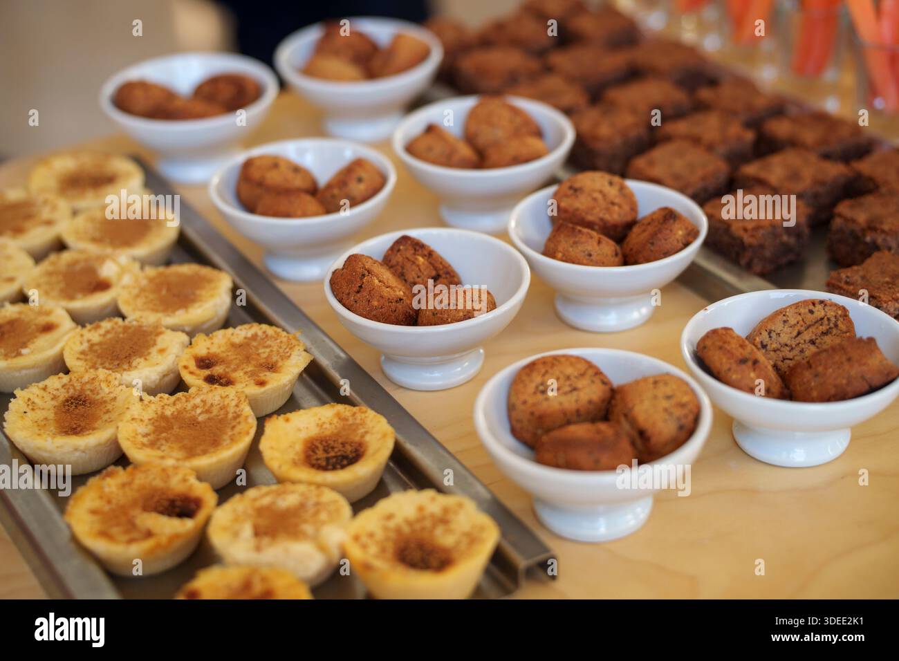 Verschiedene Mini-Torten und kleine gebackene Leckereien, die in Schüsseln und Tabletts auf einem Holztisch bei einem Buffet oder einer Veranstaltung ausgestellt werden Stockfoto
