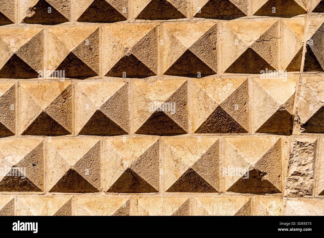 Aus nächster Nähe eine strukturierte Steinmauer mit einem Muster aus Pyramidenformen, das Erdtöne und Schatten zeigt Stockfoto