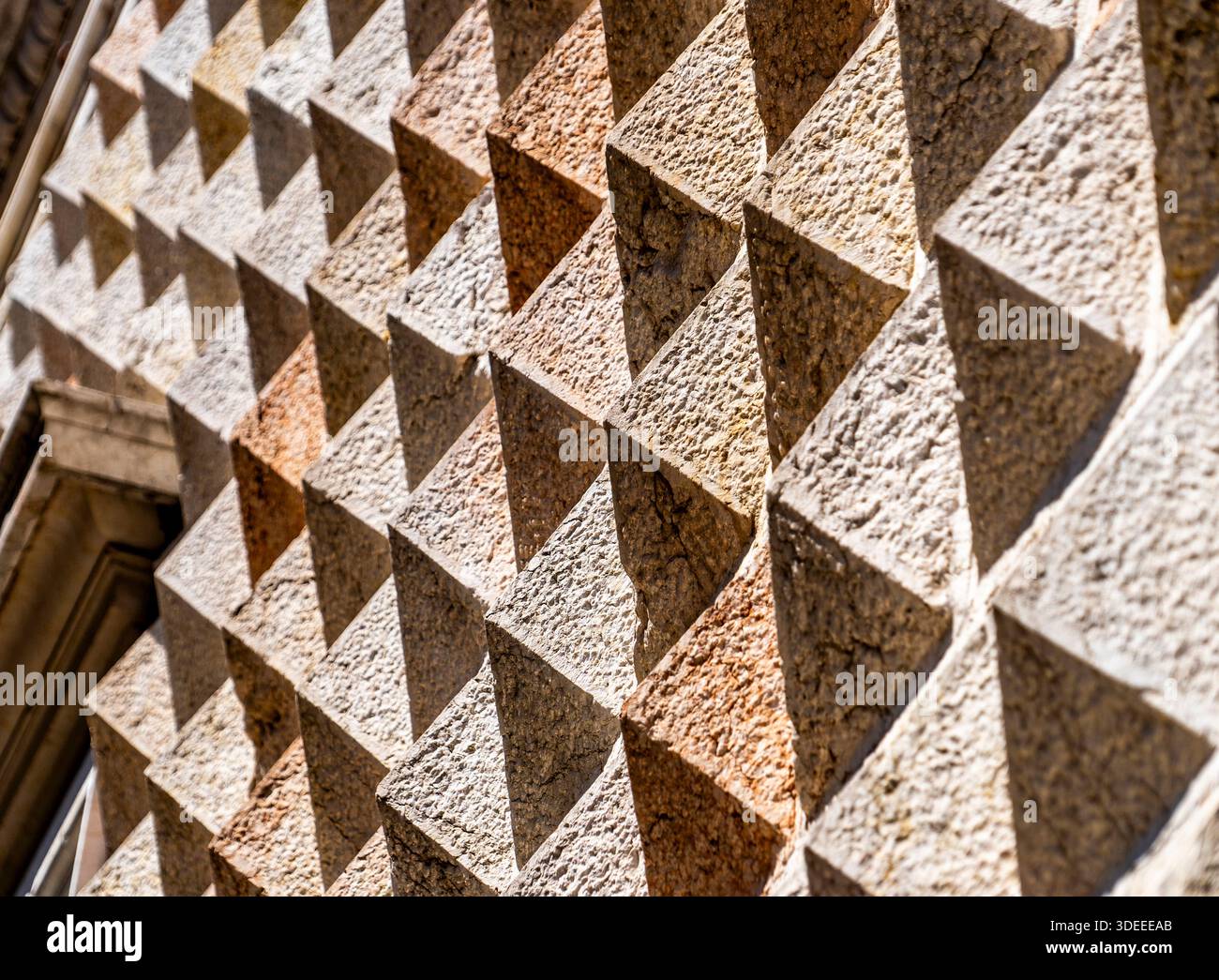 Eine strukturierte Wand mit einem dreidimensionalen Dreiecksmuster, die in verschiedenen Beige- und Brauntönen gehalten wird, mit Schatten durch Sonnenlicht Stockfoto