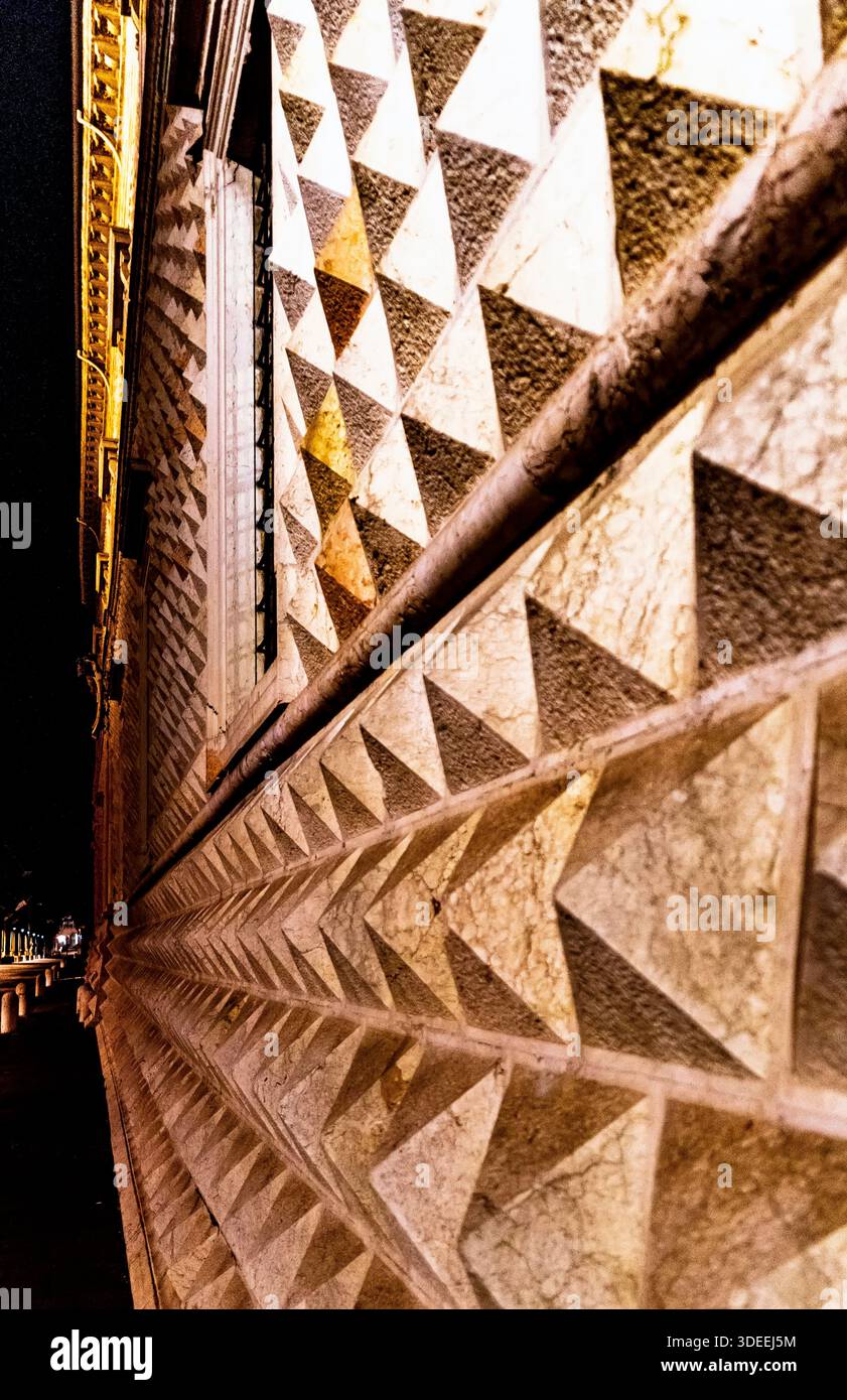 Nahaufnahme einer strukturierten Wand mit geometrischem Dreiecksmuster, beleuchtet bei Nacht Stockfoto