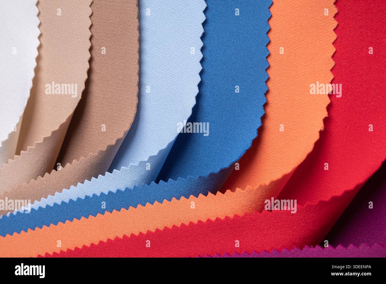 Studio-Nahaufnahme mit farbenfrohen Stoffmustern in geschwungenen Falten, die lebendige und pastellfarbene Töne mit gepinkten Kanten zeigen. Ideal für Textildesign... Stockfoto