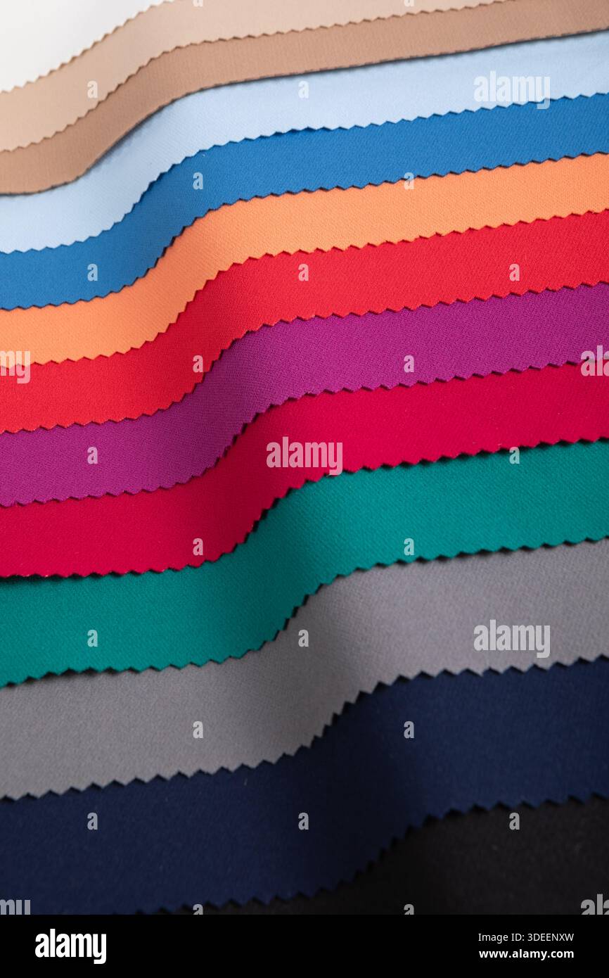 Studio-Nahaufnahme mit farbenfrohen Stoffmustern in geschwungenen Falten, die lebendige und pastellfarbene Töne mit gepinkten Kanten zeigen. Ideal für Textildesign... Stockfoto