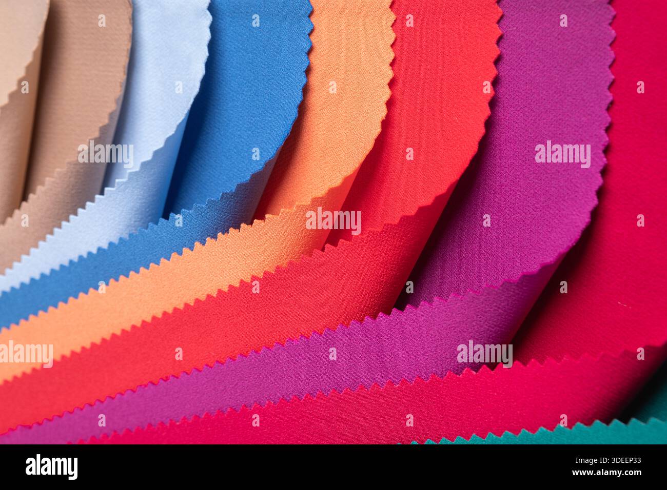Studio-Nahaufnahme mit farbenfrohen Stoffmustern in geschwungenen Falten, die lebendige und pastellfarbene Töne mit gepinkten Kanten zeigen. Ideal für Textildesign... Stockfoto