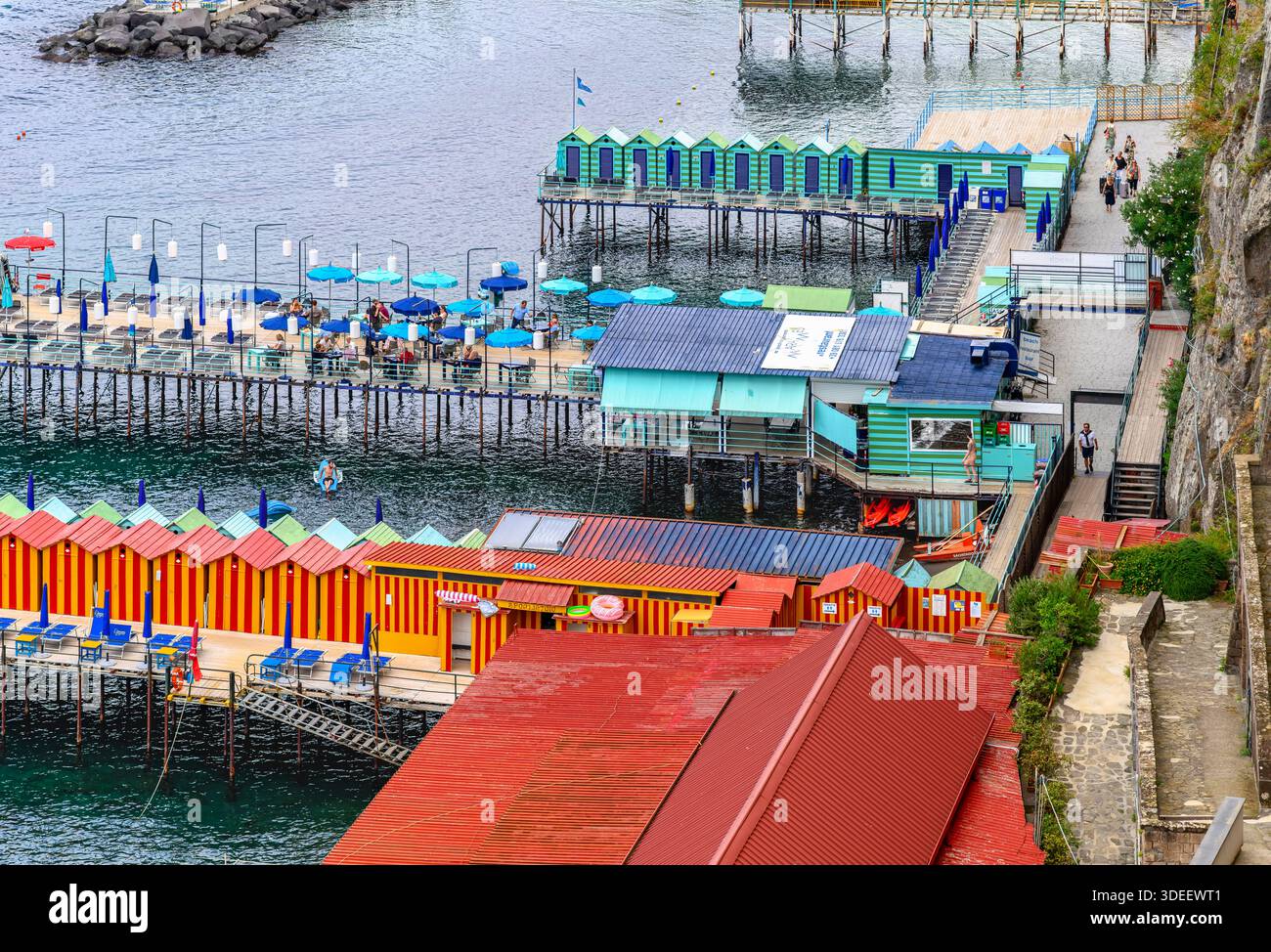 Blick hinunter auf den privaten Bereich von Sorrent am Meer Bagni Salvatore. Mit Touristen, Liegestühlen, Sonnenschirmen, Badehütten, Ruderbooten und Kajaks. Stockfoto