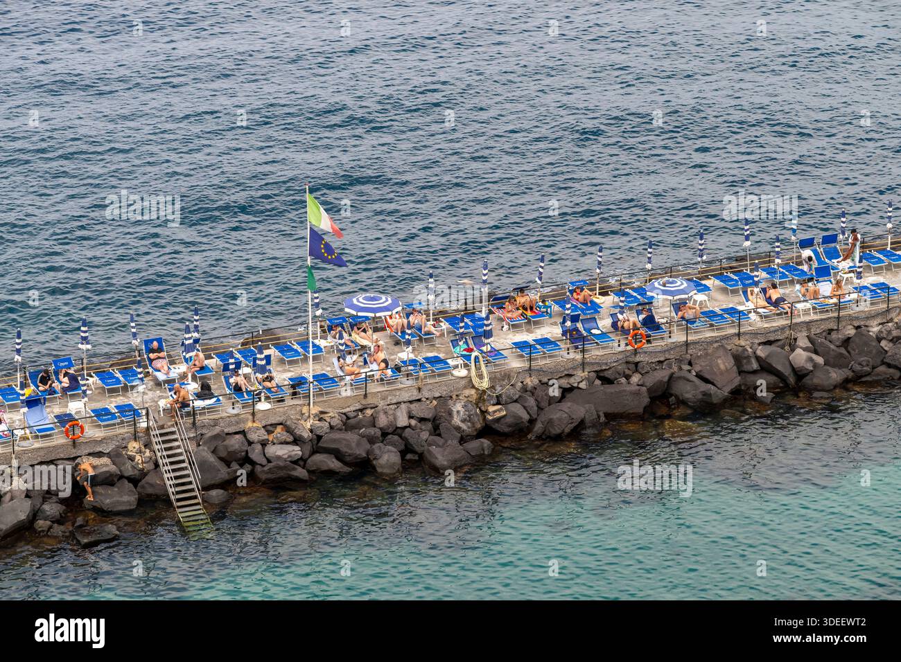 Blick hinunter auf den privaten Bereich von Sorrent am Meer Bagni Salvatore. Mit Touristen, Liegestühlen, Sonnenschirmen, Badehütten, Ruderbooten und Kajaks. Stockfoto