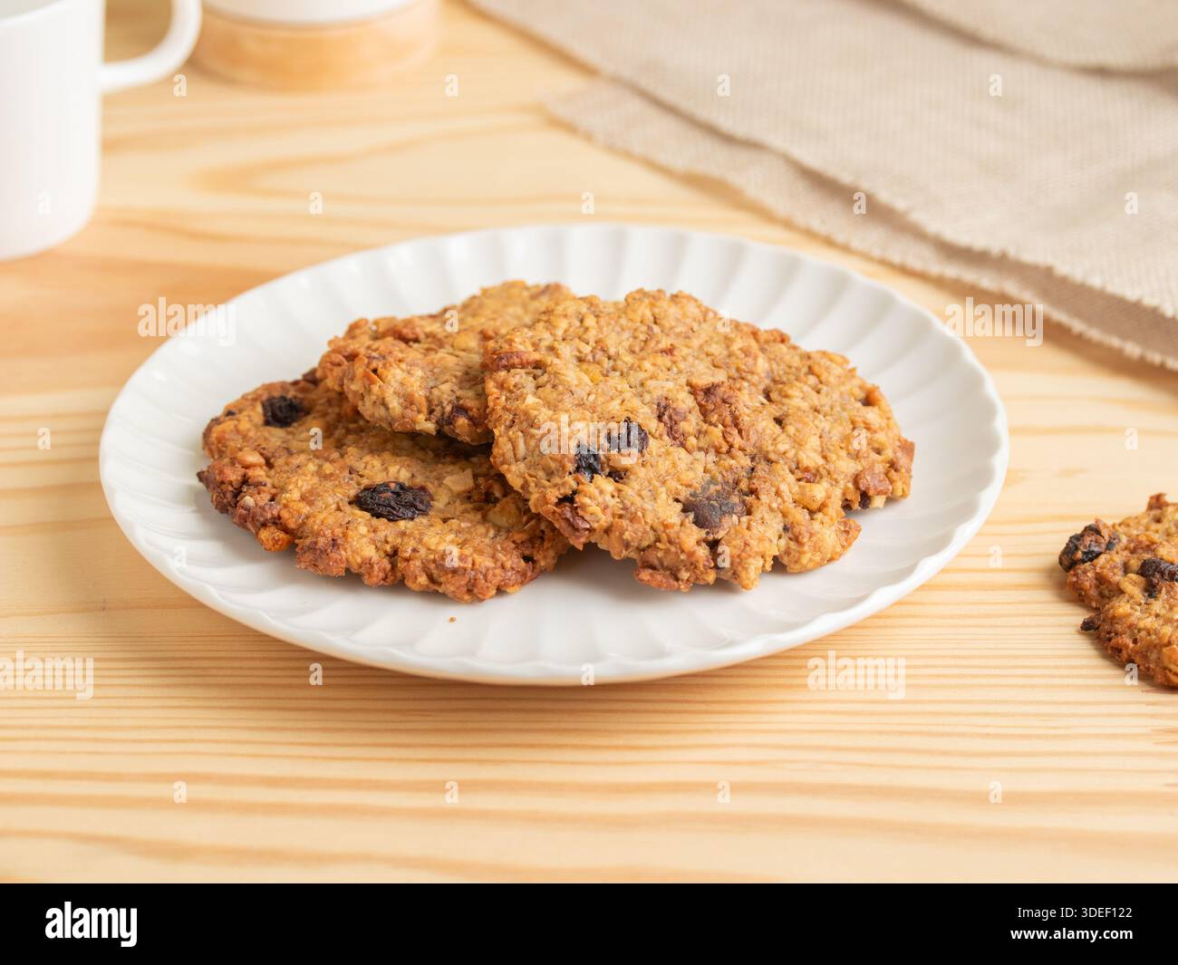 Frisch gebackene Haferflocken mit Rosinenkeksen auf einem weißen geriffelten Teller auf einem Holztisch. Kaugummi, süße Leckereien aus Hafer, Rosinen und klassischem Backofen Stockfoto