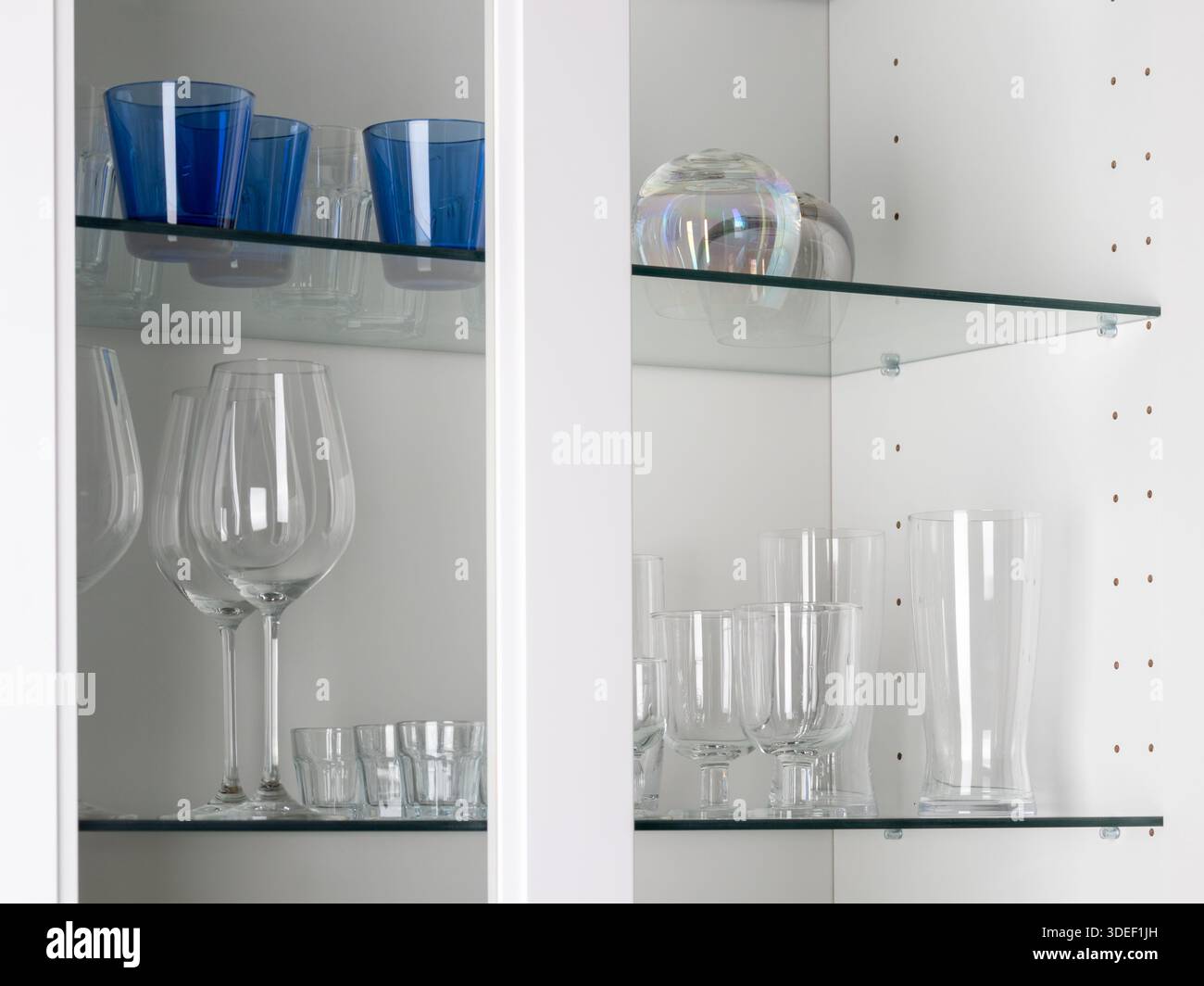 Organisierter Schrank mit verschiedenen Trinkgläsern, darunter blaue Gläser, große Weingläser und kleine klare Gläser. Stilvolle Hausbar oder Küche Stockfoto