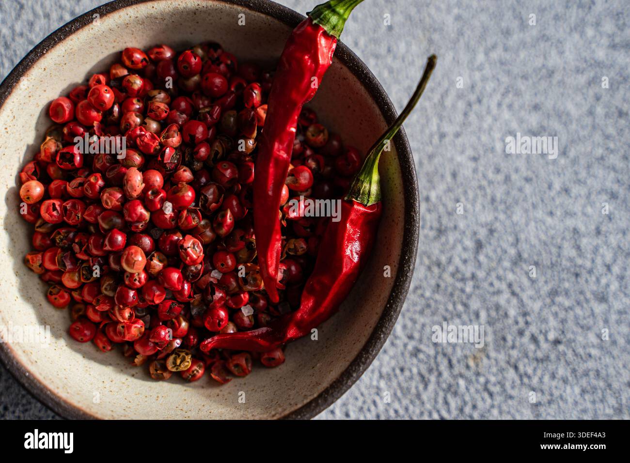 Blick von oben auf eine Schüssel mit frischen rosa Pfefferkörnern und getrockneten roten Chilis auf einem Tisch Stockfoto