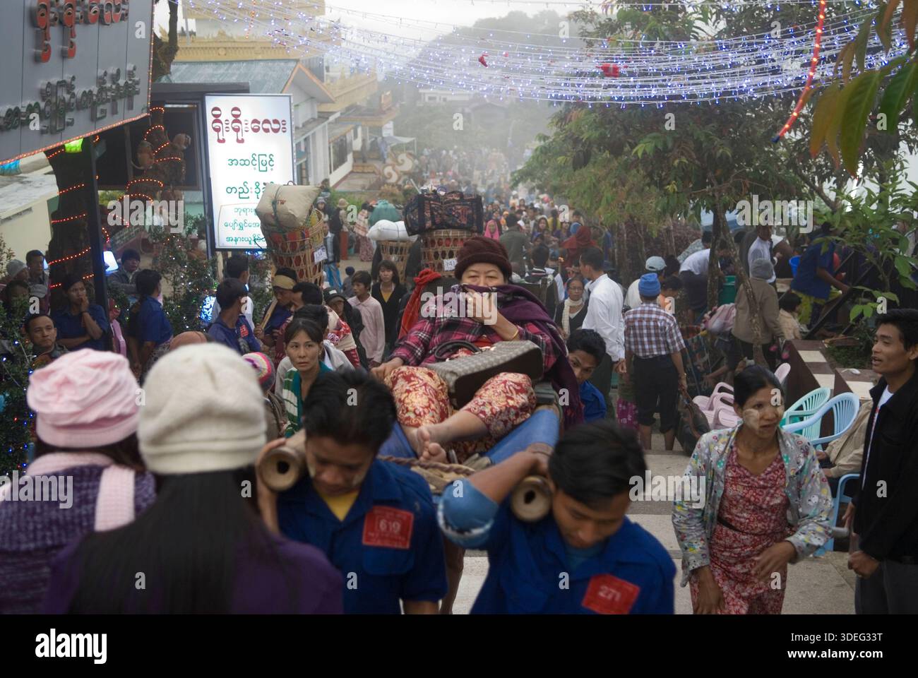 Träger tragen eine ältere Frau den Berg hinauf zum Golden Rock Tazaungdaing Festival auf einer traditionellen Bambustrage, die manchmal als hölzernes Streichbett oder einfach nur als Trage bezeichnet wird, Myanmars Festival of Lights. Ein buddhistisches fest am Ende der Regenzeit, wo der heilige Goldene Felsen zu einem wichtigen Wallfahrtsort wird. Kyaiktiyo, Mons State, Myanmar 9. November 2011 2010, HOMER SYKES Stockfoto