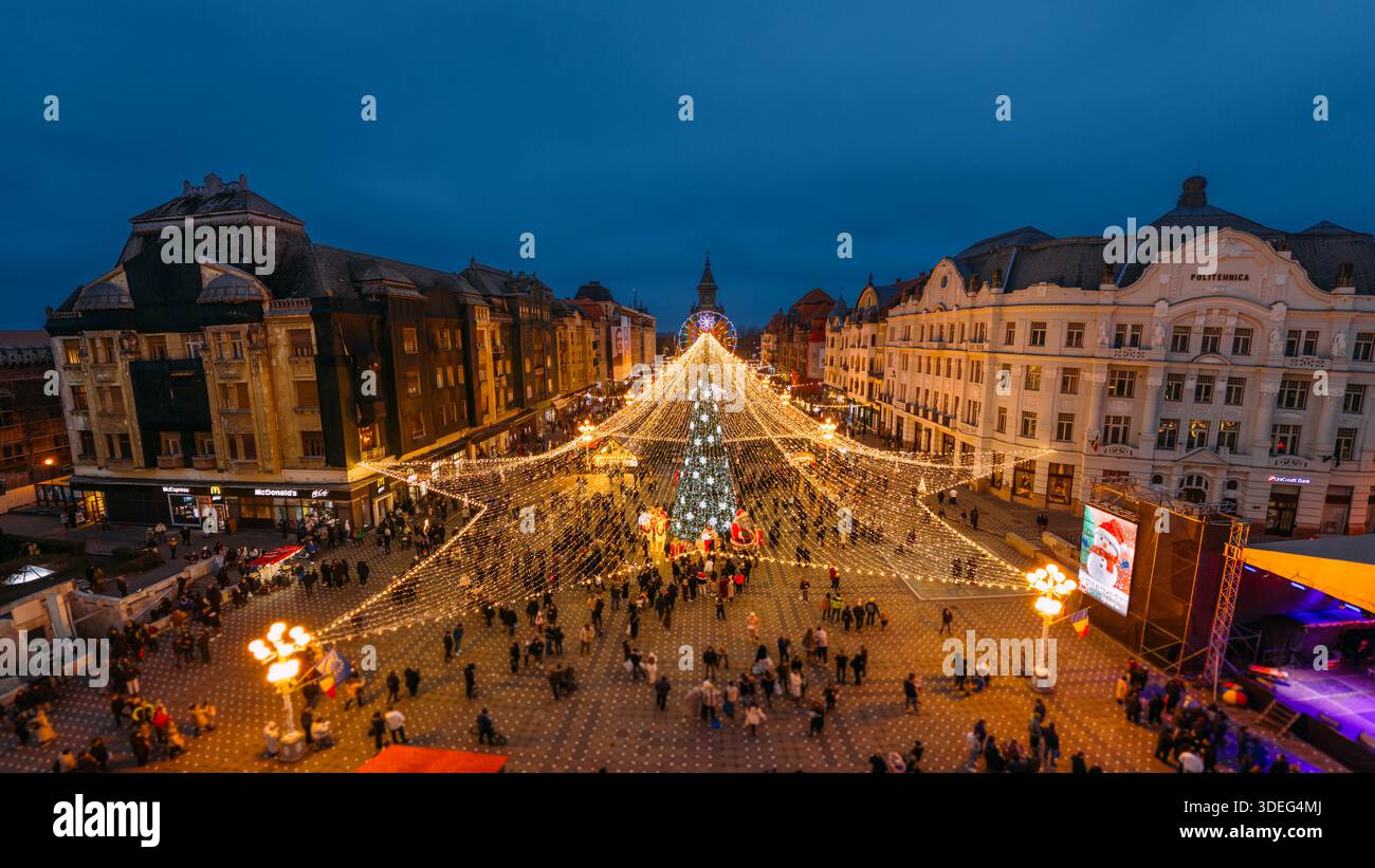 Aus der Vogelperspektive funkeln die Weihnachtslichter wie Sterne über einem belebten Platz und beleuchten die historischen Gebäude rund um Piața Victoriei, Timișoara, Ti Stockfoto