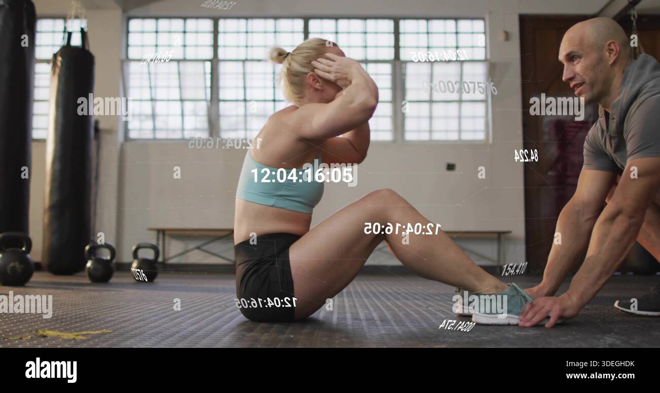 Beim Sit-ups trage der Trainee im Fitnessstudio Ausrüstung, der Trainer hält die Füße mit Kettlebells, Zeitstempel-Overlay Stockfoto