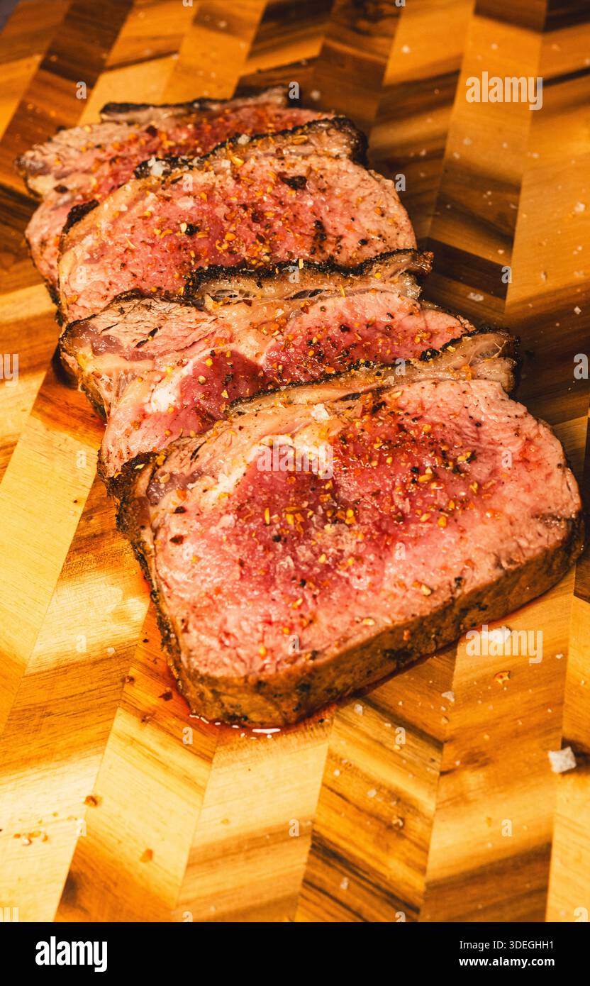 Topside Rinderbraten mit Gewürzstreifen beschichtet, innen geröstet selten und saftig, in Scheiben geschnitten und auf einem Holzbrett präsentiert. Zart, geschmackvoll und elegant geschnitzt Stockfoto
