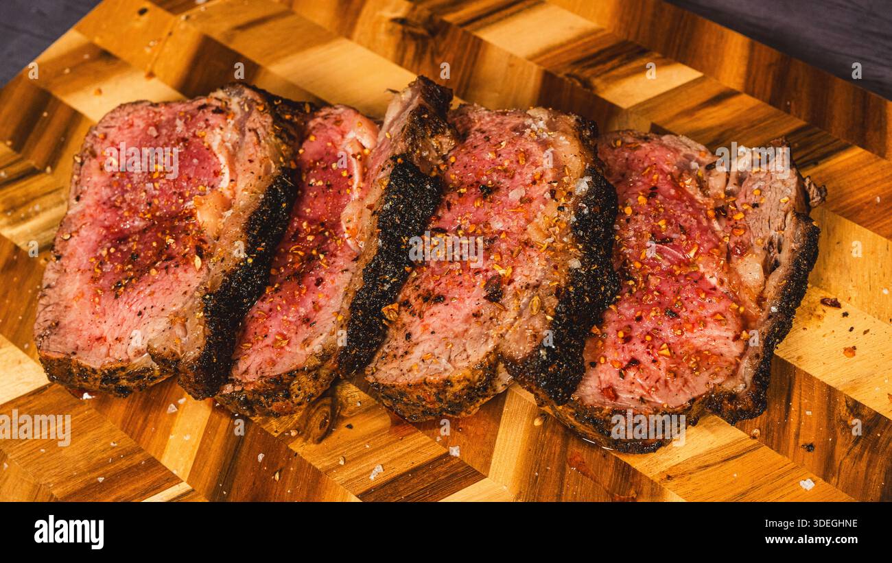 Topside Rinderbraten mit Gewürzstreifen beschichtet, innen geröstet selten und saftig, in Scheiben geschnitten und auf einem Holzbrett präsentiert. Zart, geschmackvoll und elegant geschnitzt Stockfoto