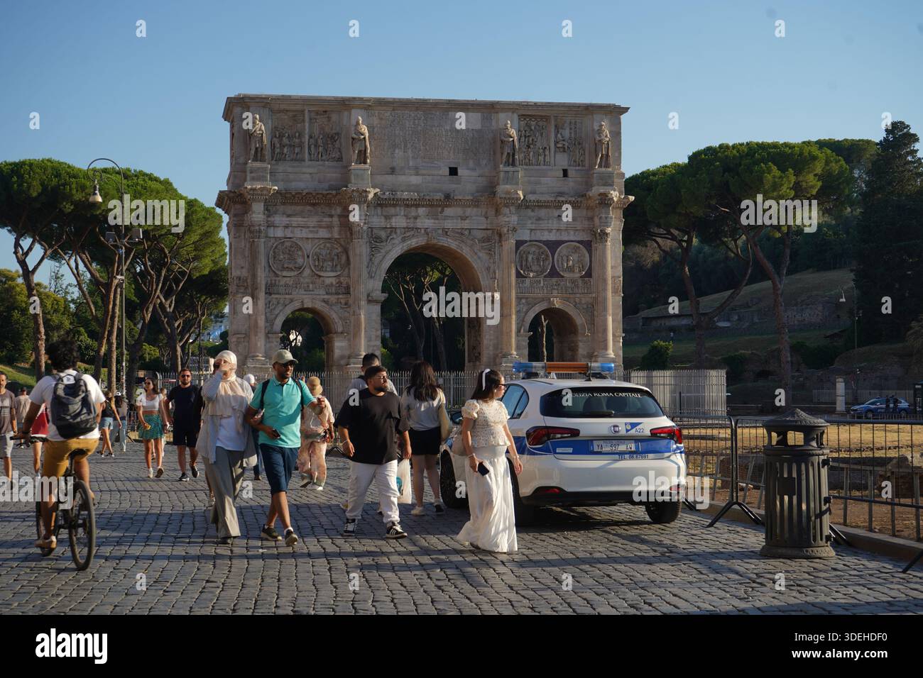 Touristenmassen, die am Konstantinsbogen in der Nähe des Kolosseums vorbeilaufen. Ein Auto der Polizia Roma Capitale ist sichtbar. Sonniger Sommertag in der Ewigen Stadt. Stockfoto