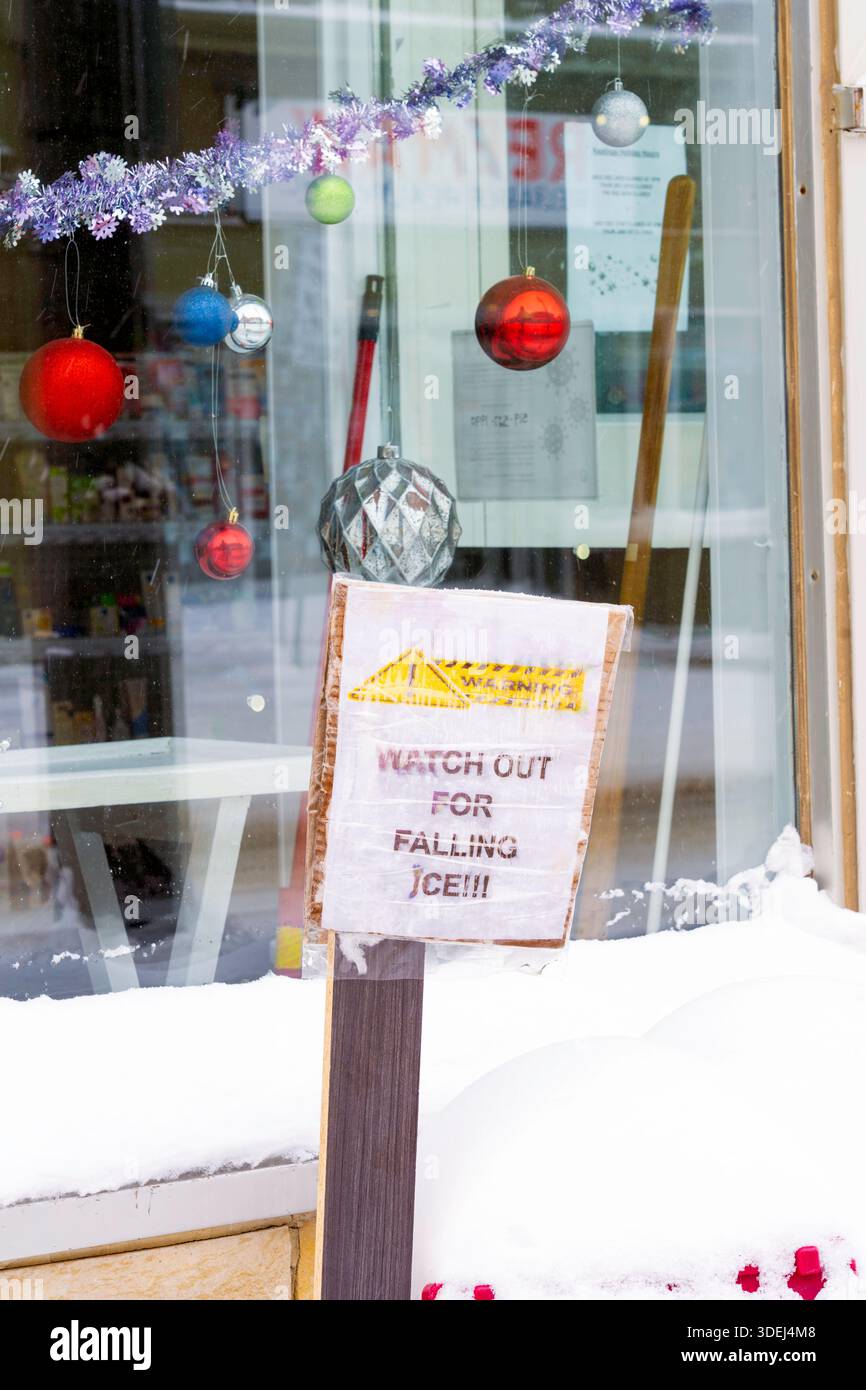 Ein Schild vor der Ladenfront warnt die Öffentlichkeit, dass Eis vom Dach fällt. Januar 2026. Stockfoto