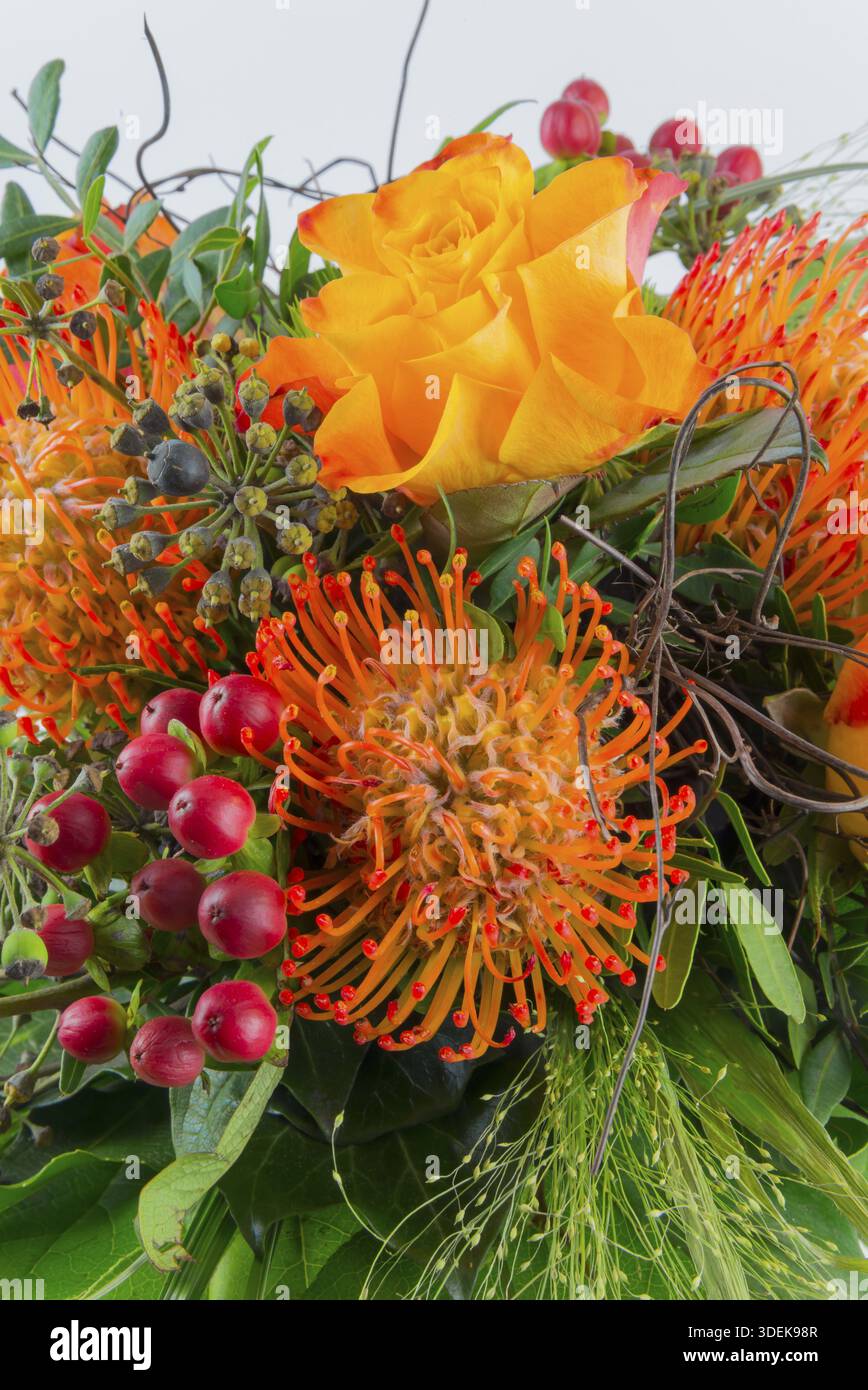 Farbenfrohes Bouquet mit orangen und gelben Blumen, umgeben von roten Beeren und grünem Laub, Protea und Rose Stockfoto