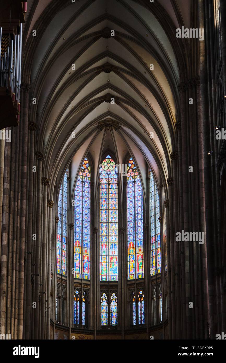 Faszinierender Blick in eine gotische Kathedrale mit majestätischer Gewölbedecke und einem komplizierten Buntglasfenster. Stockfoto