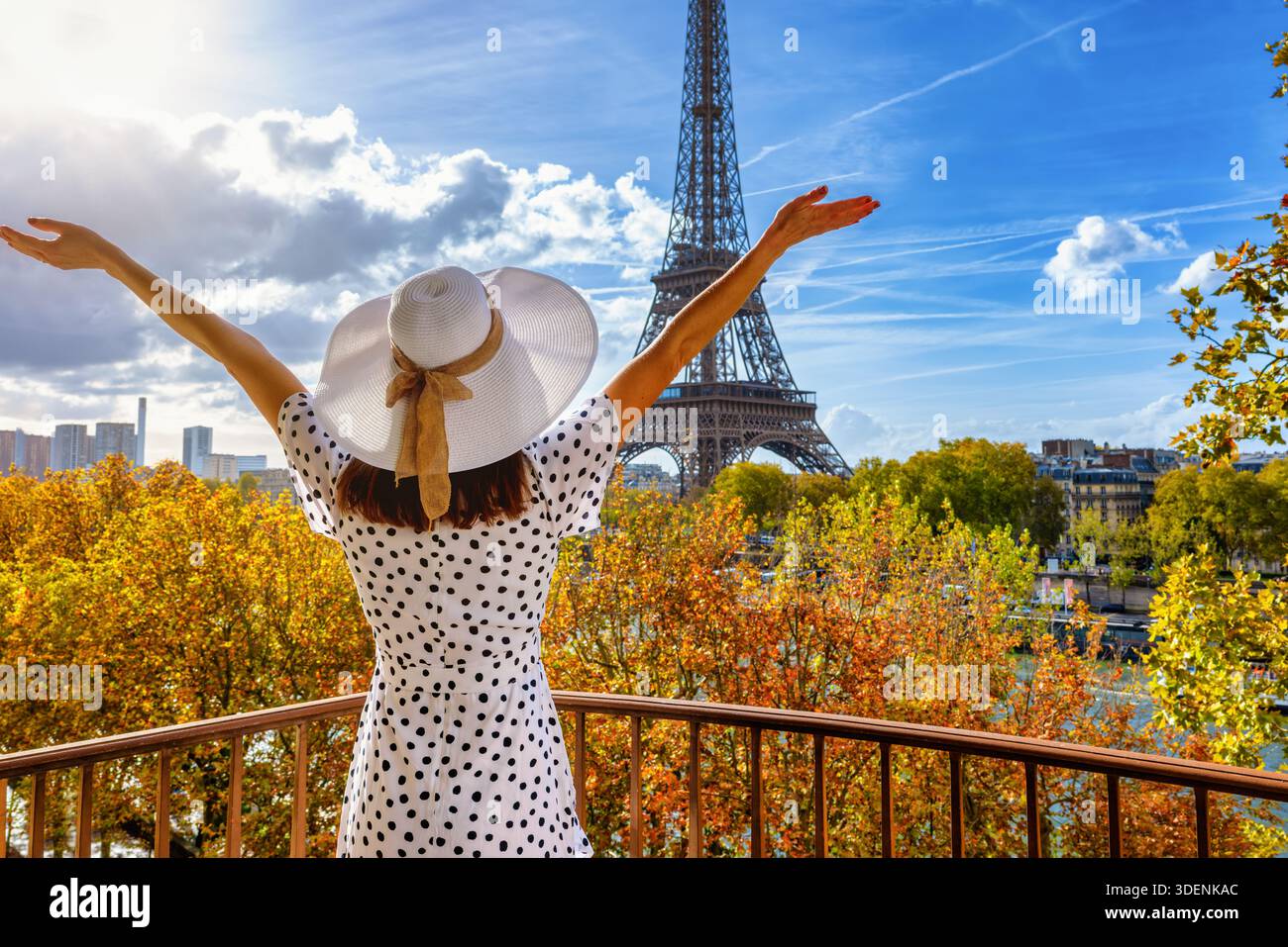 Rückansicht einer glücklichen Frau in einem weißen Kleid, die während eines suny-Tages vom Balkon aus den Blick auf den Eiffelturm in Paris, Frankreich, genießt Stockfoto