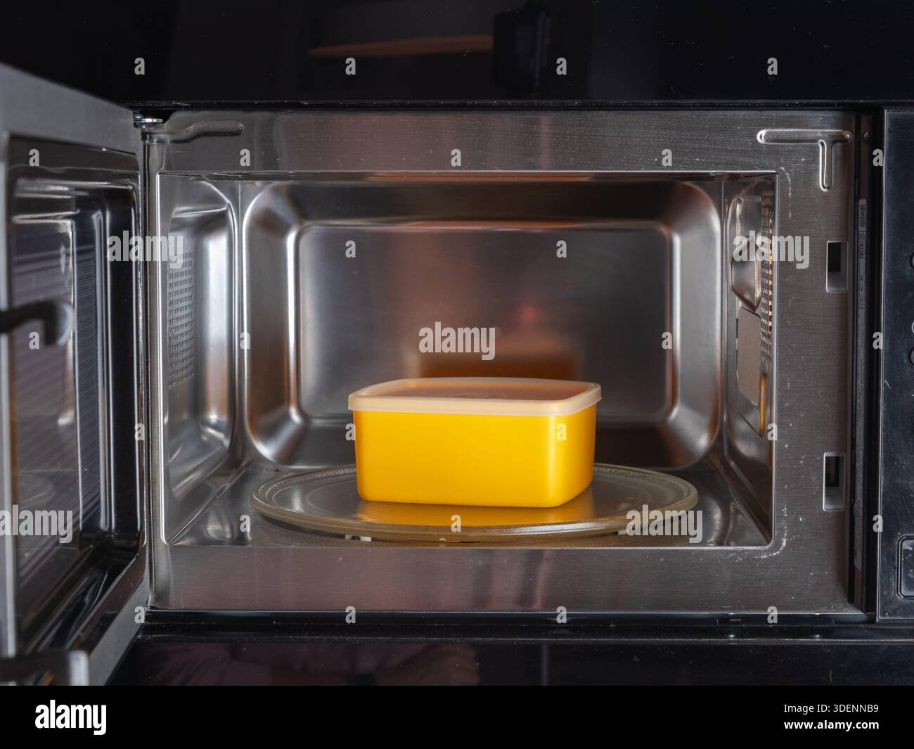 Ein Mikrowellenherd enthält einen Behälter mit Deckel im Inneren, der das sichere und praktische Erwärmen oder Aufwärmen von Lebensmitteln in einer modernen Küchenumgebung veranschaulicht Stockfoto