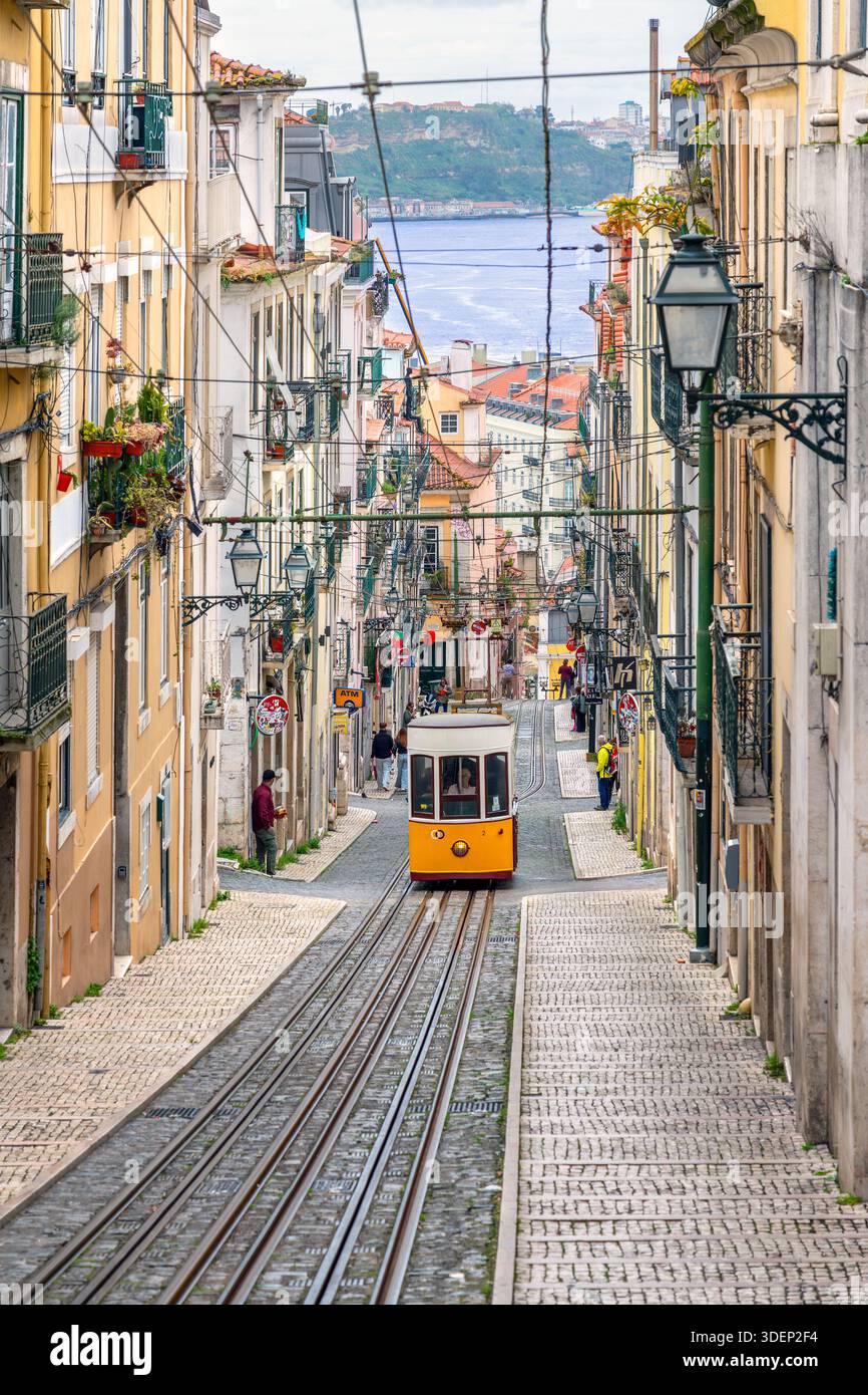 Traditionelle alte gelbe Straßenbahn an der Straßenbahnlinie 28, die steile Kopfsteinpflasterstraße in der Hauptstadt Lissabon/Lisboa, Portugal, hinaufsteigt Stockfoto