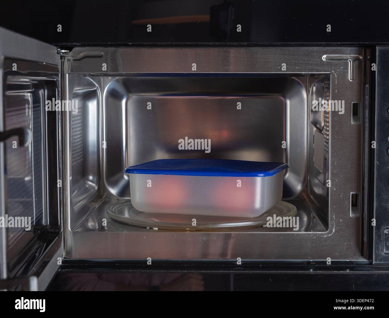 Ein Mikrowellenherd enthält einen Behälter mit Deckel im Inneren, der das sichere und praktische Erwärmen oder Aufwärmen von Lebensmitteln in einer modernen Küchenumgebung veranschaulicht Stockfoto