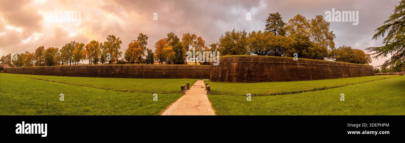 Murallas históricas de Lucca, Italia, Rodeadas de césped y árboles otoñales, con sendero Central y cielo Dramático al atardecer. Stockfoto