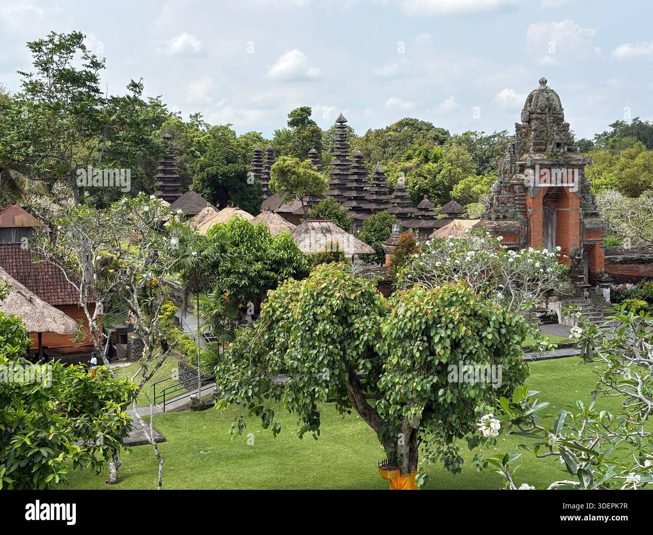 Traditioneller balinesischer Tempelkomplex mit gestuften Pagodendächern, Steintor und üppigem tropischem Garten in Bali, Indonesien Stockfoto