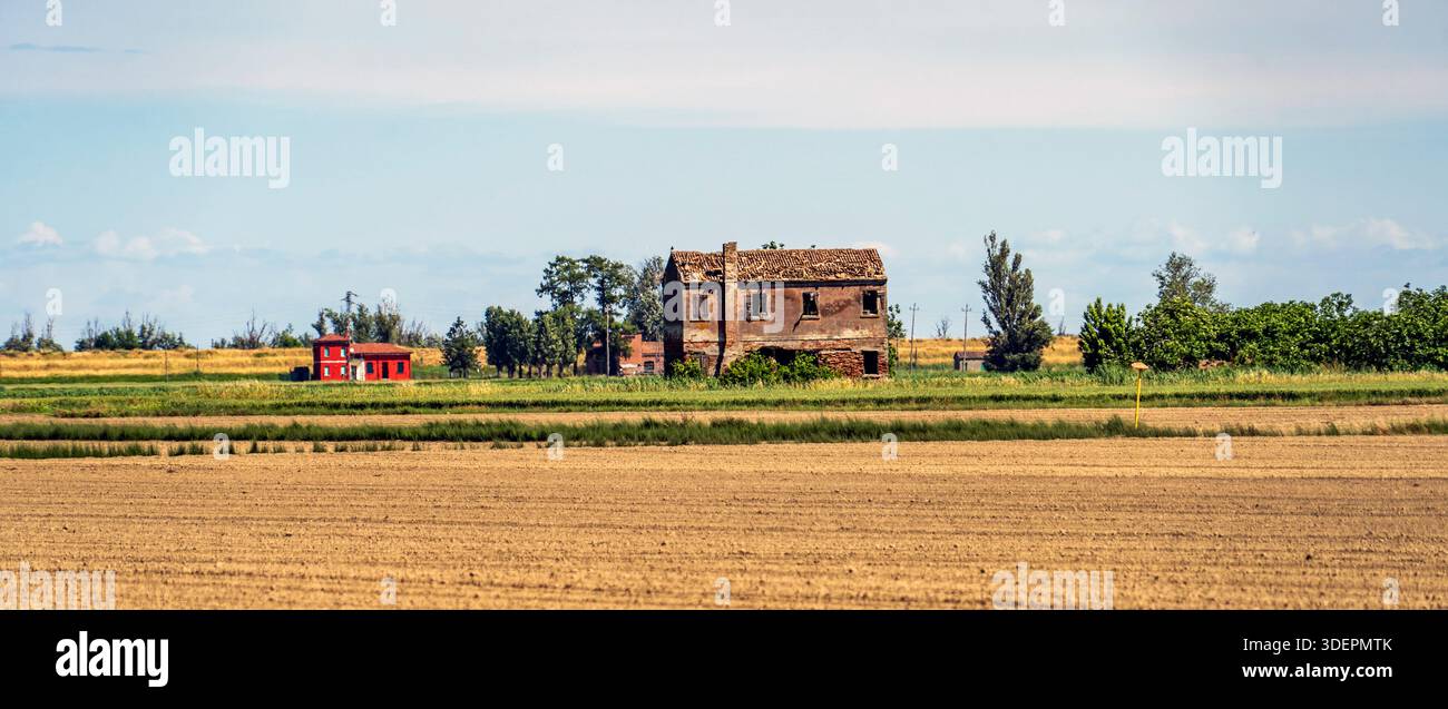 Verlassenes Bauernhaus und rote Scheune in einer ländlichen Landschaft mit Feldern. Stockfoto