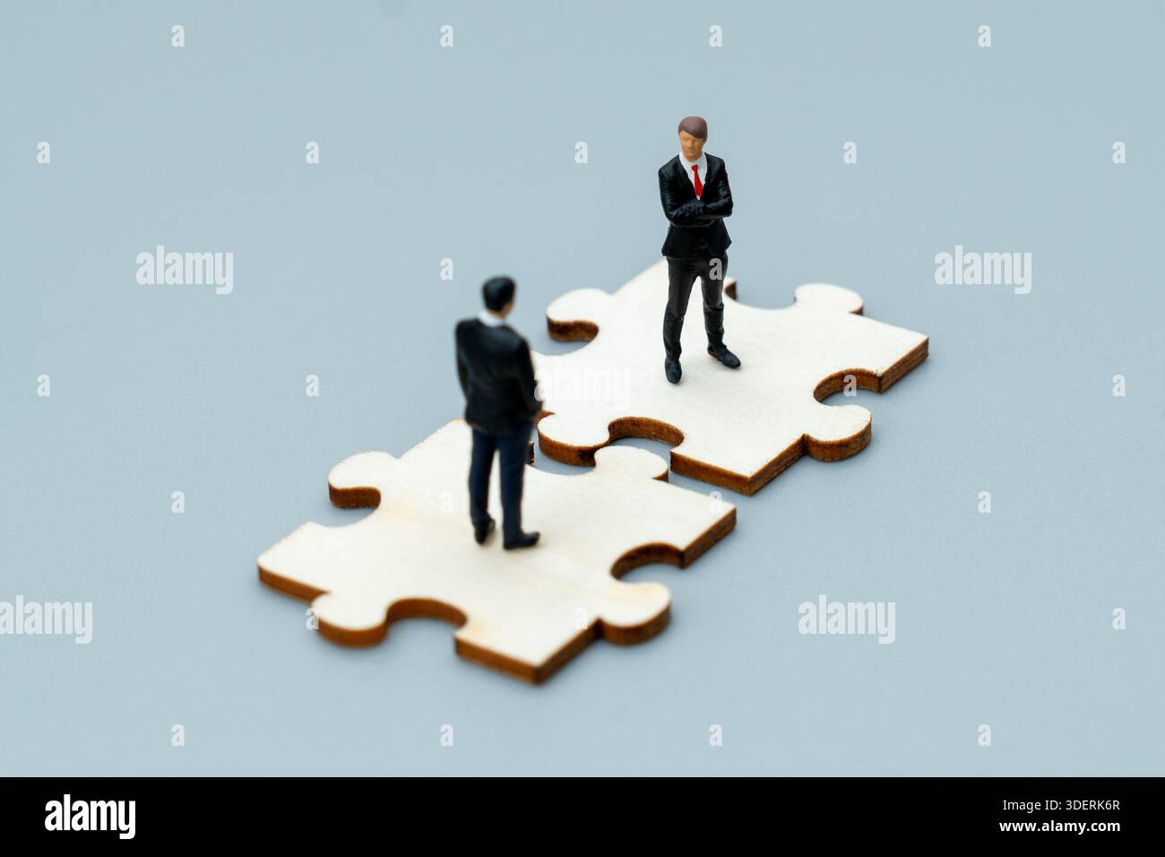 Kleine Geschäftsfiguren stehen auf ineinander greifenden Puzzleteilen. Unternehmenspartnerschaft, Teamarbeit, strategisches Collaboration-Konzept. Stockfoto