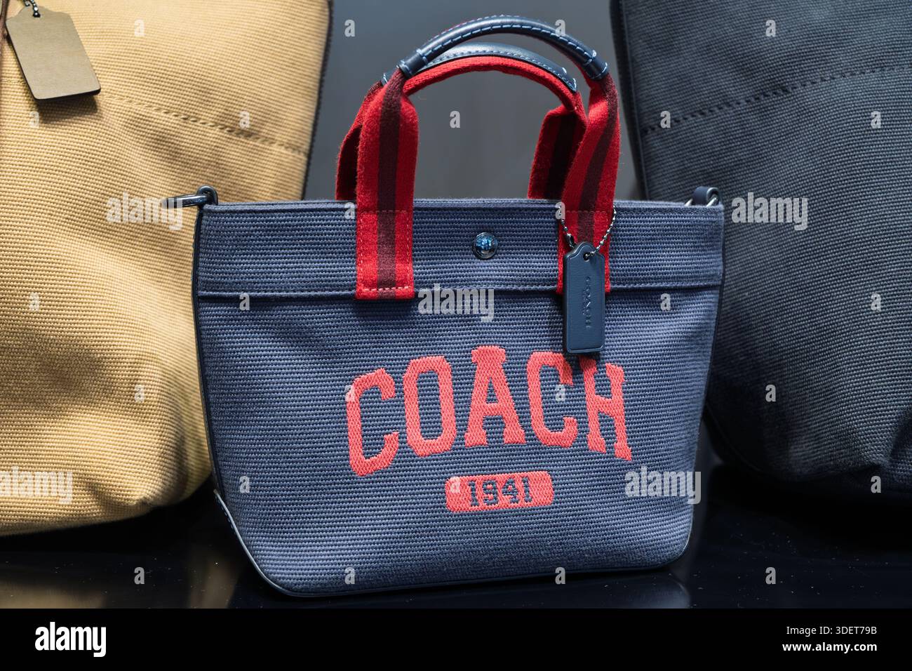 Penang, Malaysia - 16. Oktober 2025: Eine Coach Tragetasche aus marineblauem Stoff mit kontrastierenden roten Trägern und Logo auf einer schwarzen Oberfläche Stockfoto