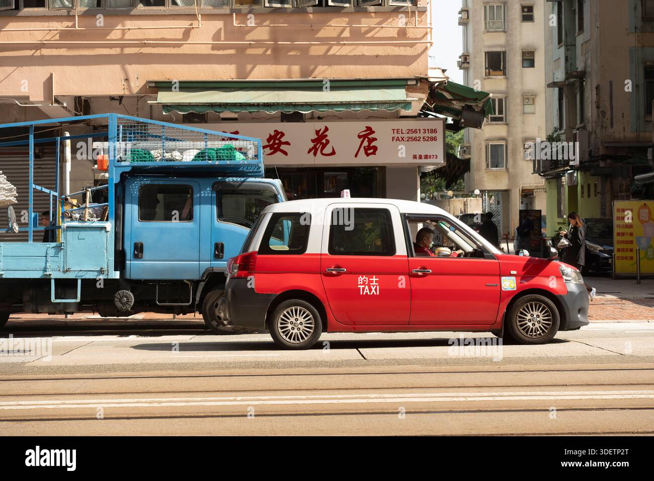 Ein rotes Taxi und ein blauer Truck auf einer Straße in Hongkong, nahe North Point Stockfoto