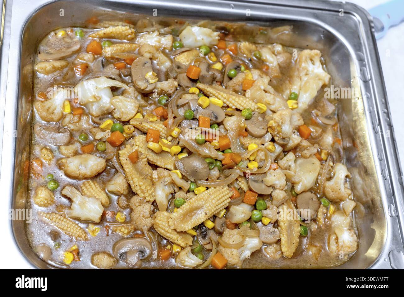 Eine Nahaufnahme eines großen Metalltabletts mit einer köstlichen und farbenfrohen Gemüsepfanne mit Pilzen, Blumenkohl, Babymais, Erbsen und c Stockfoto