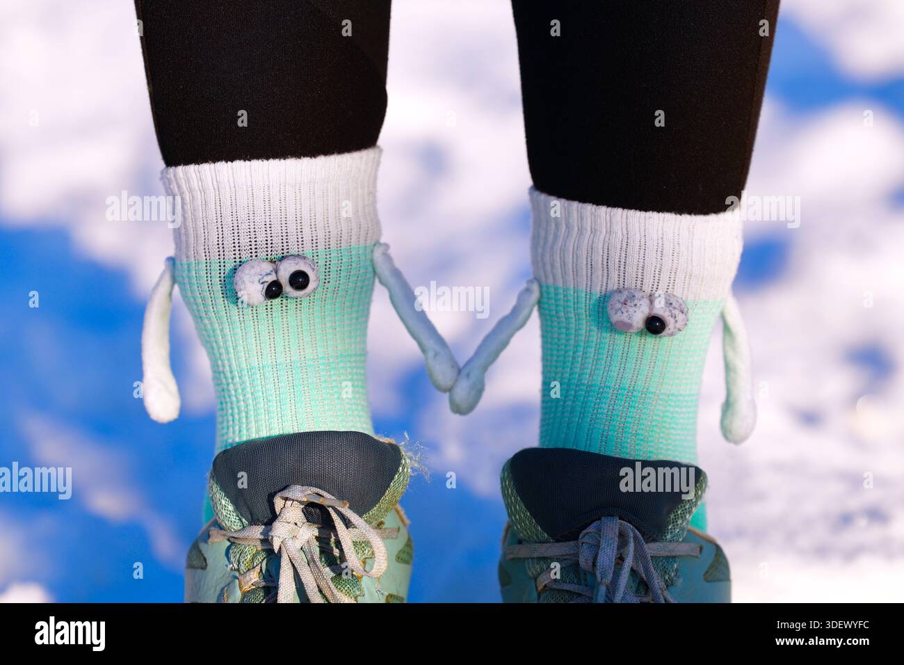 Verspielte Monster Socken mit Figuren, die Hände halten, und Laufschuhe im Winterschnee Stockfoto