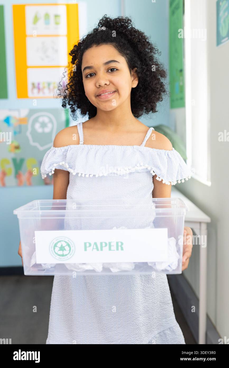 Afroamerikanischer Teenager, der in der Klasse steht und einen PAPIERKORB mit zerknittertem Papier in einem gerafften Kleid hält Stockfoto