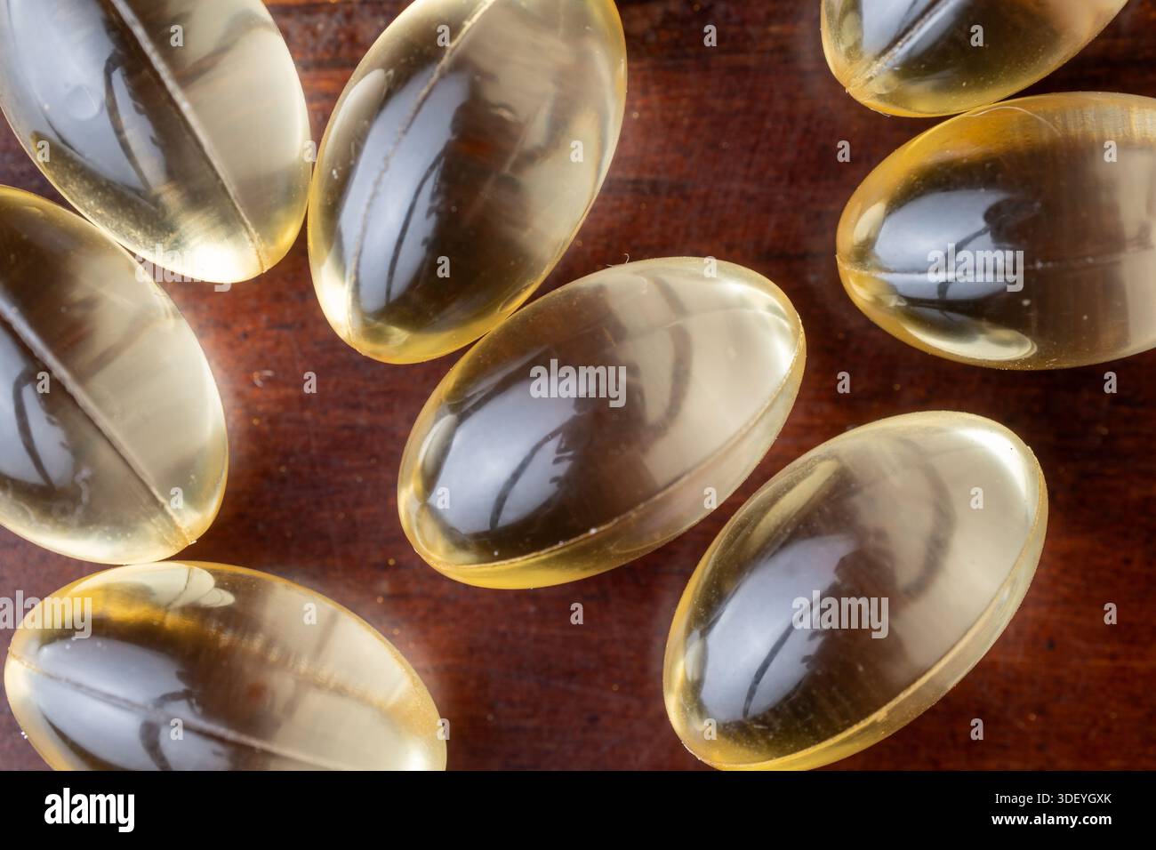 Makroaufnahme gelber flüssiger Vitaminkapseln auf braunem Holzhintergrund. Konzept von Nahrungsergänzungsmitteln, täglicher Gesundheitsversorgung und Wellness-Routine. Stockfoto
