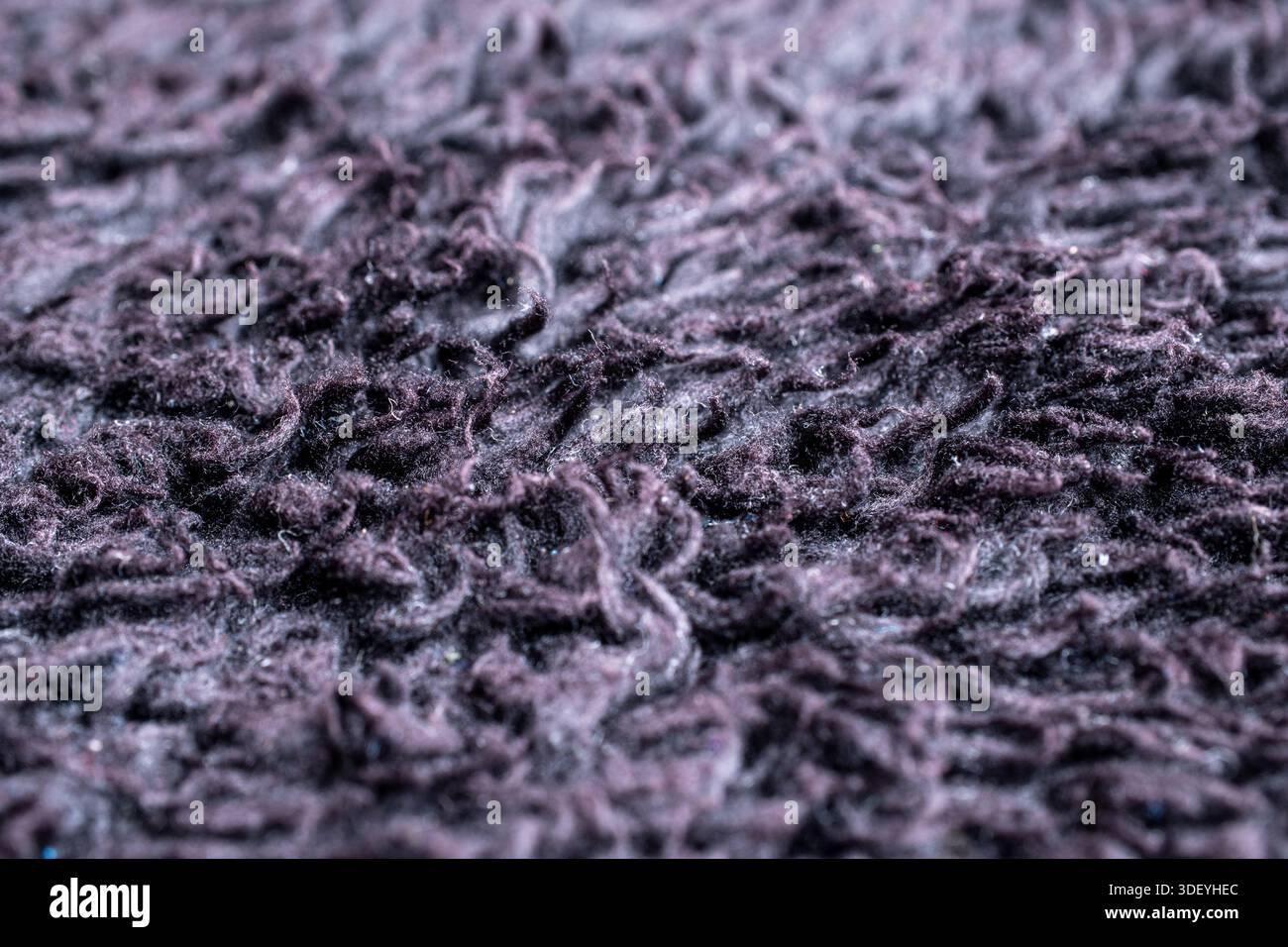 Extreme Nahaufnahme tiefvioletter synthetischer Teppichfasern. Detaillierte, weiche, haarige Textur und unordentliches Stapelmuster für das Hintergrundkonzept der Inneneinrichtung. Stockfoto
