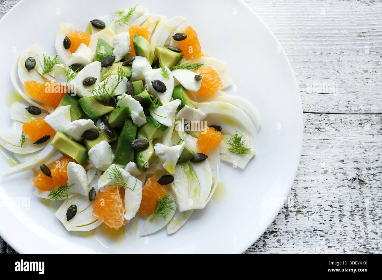 Frischer Salat aus Fenchel, Orangen, Avocado, Käsestücken und Kürbiskernen, mit extra nativem Olivenöl auf weißem hölzernem Hintergrund gekleidet. Stockfoto
