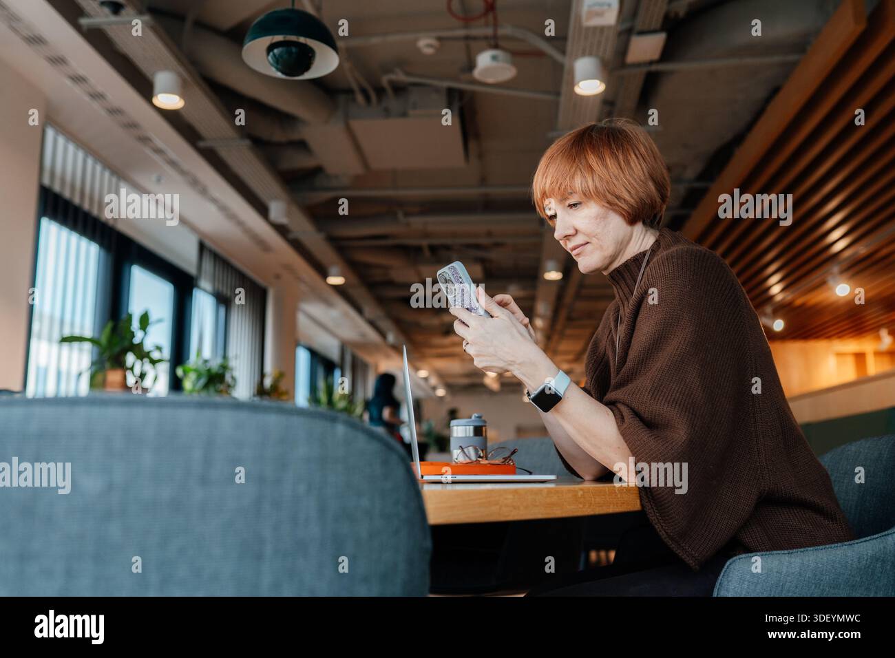 Reife weibliche Prüfung von Nachrichten, während sie im freigegebenen Workspace sitzen Stockfoto