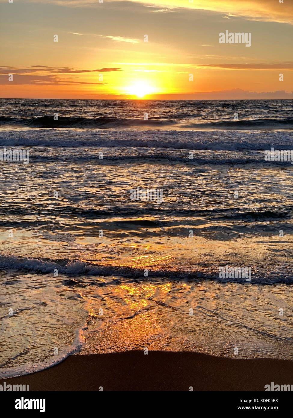 Meereswellen bei Sonnenaufgang, goldenes Licht reflektiert auf dem Wasser und bunte Wolken am Himmel - Smartphone-aufgenommenes Stockfoto