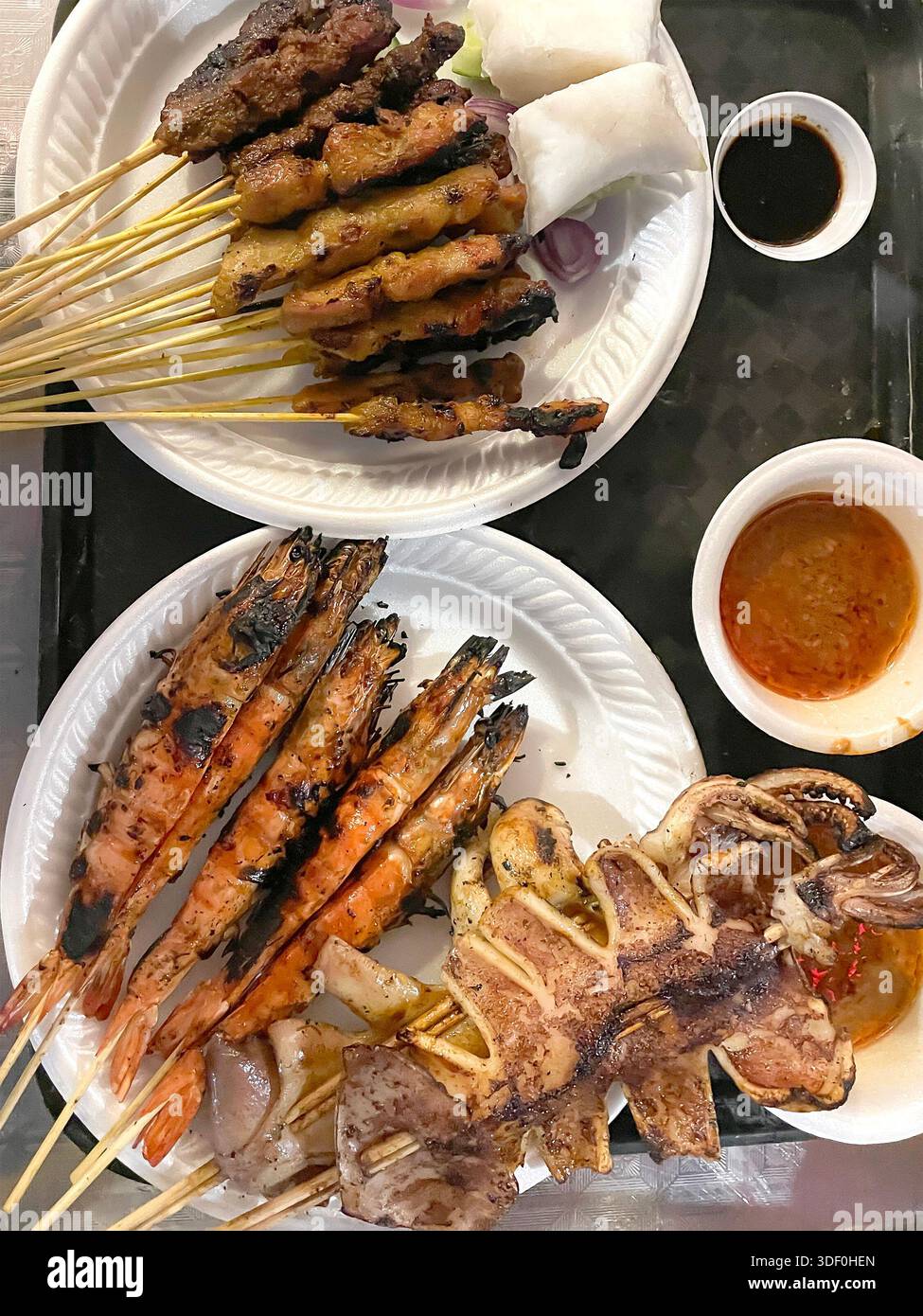 Gegrillte Meeresfrüchte- und Fleischspieße auf Papiertellern mit eintauchenden Saucen in einem Street Food Stall oder einem zwanglosen Restaurant singapur asia Stockfoto